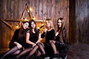 Four cute friends girls wear black dresses against large light christmas star decoration on wooden background. photo