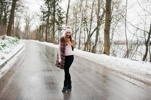 Stylish girl in fur coat and headwear at winter day on road. photo
