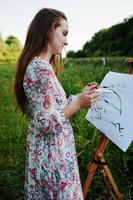 Portrait of an attractive young woman in long dress painting with watercolor in nature. photo