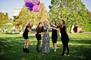 cinco chicas visten de negro con globos bebiendo champán rojo en la despedida de soltera. foto