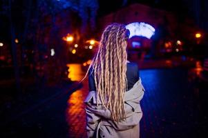 Girl with dreadlocks walking at night street of city against garland lights. photo