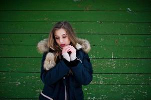 Beautiful brunette girl in winter warm clothing. Model on winter jacket against green wooden background. photo