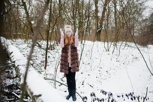 chica elegante con abrigo de piel y sombreros en el bosque de invierno. foto