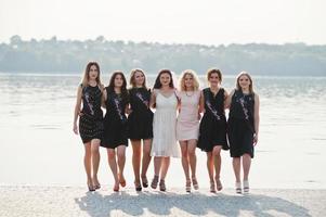 grupo de 7 chicas visten de negro y 2 novias en despedida de soltera contra la playa soleada. foto