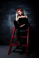 Fashion model red haired girl with originally make up like leopard predator against steel wall. Studio portrait on ladder. photo