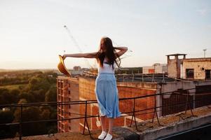 Portrait of a lovely girl in casual clothing posing on the roof with her hat in her hand at the sunset. photo