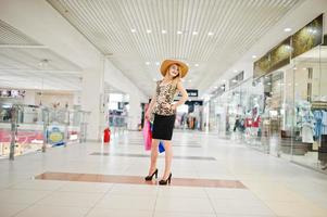 retrato de una atractiva joven con blusa de leopardo, falda negra posando con un sombrero y bolsas de compras. foto