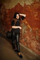 Fashion outdoor photo of gorgeous sensual woman with dark hair in elegant clothes and luxurious fur coat at old street with grunge walls.