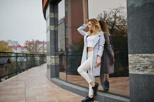 Stylish curly blonde model girl wear on white with mobile phone at hand posing against large window. photo