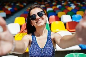 retrato de primer plano de una hermosa chica en forma con gafas de sol sentada en el estadio. foto