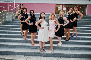 Group of 8 girls wear on black and 2 brides at hen party stay on stairs. photo