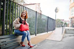 chica pelirroja con bolso rojo posado en un banco. foto