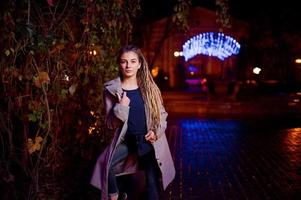 chica con rastas caminando por la calle nocturna de la ciudad contra las luces de la guirnalda. foto