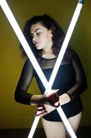 Curly brunette plus size model with two long led lamp against yellow wall. photo