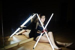 Curly brunette plus size model with two long led lamp at dance room with mirror. photo