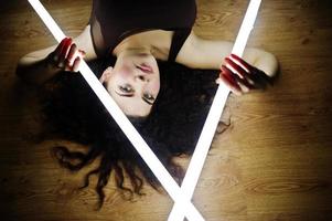 Curly brunette plus size model with two long led lamp at black room lying on flat. photo