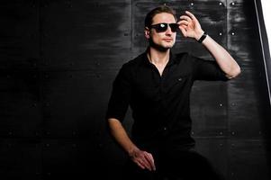 Studio portrait of stylish man wear on black shirt and glasses against steel wall. photo