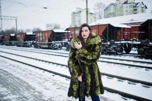 chica morena con abrigo de piel verde en la estación de la plataforma en el día de invierno. foto