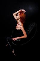 modelo de moda chica pelirroja con maquillaje original como depredador leopardo aislado en negro. retrato de estudio en silla. foto