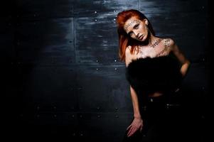 Fashion model red haired girl with originally make up like leopard predator against steel wall. Studio portrait. photo