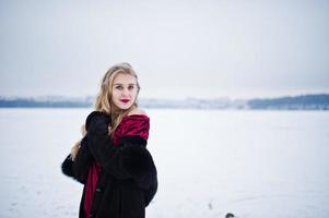 Elegance blonde girl in fur coat and red evening dress posed at winter snowy day. photo