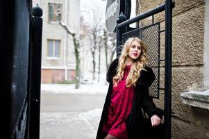 Elegance blonde girl in red evening dress and fur coat at streets of city in winter day. photo