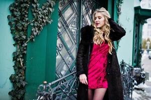 Elegance blonde girl in red evening dress and fur coat at streets of city. photo