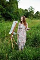 Portrait of an attractive young woman in long dress painting with watercolor in nature. photo