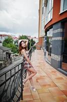 Amazing long legs with hig heels girl wear on hat posing near the railings of the modern building. photo