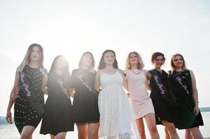 grupo de 7 chicas visten de negro y 2 novias en despedida de soltera contra la playa soleada. foto