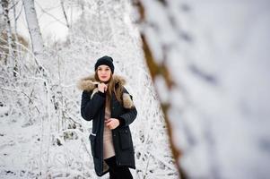 Beautiful brunette girl in winter warm clothing. Model on winter jacket and black hat. photo