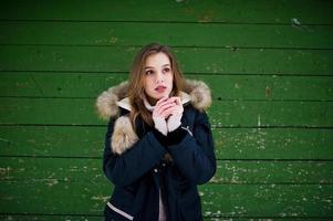 hermosa chica morena en ropa de abrigo de invierno. modelo en chaqueta de invierno sobre fondo de madera verde. foto