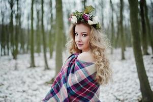 Curly cute blonde girl with wreath in checkered plaid at snowy forest in winter day. photo