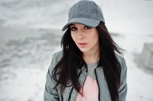 chica morena elegante con gorra gris, estilo casual de calle en el día de invierno. foto