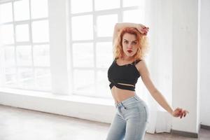 In jeans and black cloth. Attractive redhead woman posing in the spacey room near the window photo