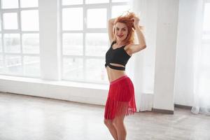 sensación fantástica para bailar solo. mujer atractiva con falda roja posando en la habitación espacial cerca de la ventana foto