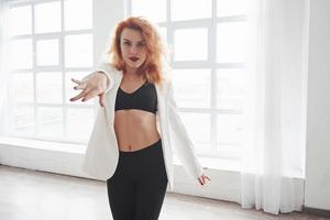 Go with me. Attractive redhead woman posing in the spacey room near the window photo