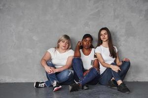 ambiente tranquilo. grupo de mujeres multiétnicas sentadas en el estudio con fondo gris foto