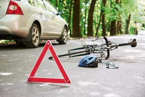 Getting hit by automobile. Bicycle and silver colored car accident on the road at forest at daytime photo