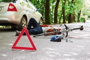 Victim on the asphalt. Bicycle and silver colored car accident on the road at forest at daytime photo