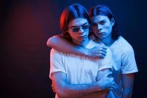 We must be together if we wanna be strong. Portrait of twin brothers. Studio shot in dark studio with neon light photo