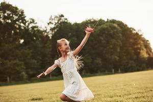 bosques detrás. chica feliz vestida de blanco diviértete con cometa en el campo. Hermosa naturaleza foto