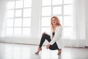 Sitting on the floor. Attractive redhead woman posing in the spacey room near the window photo