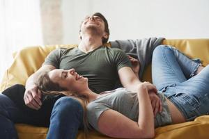 buen chiste. pareja feliz relajándose en el sofá amarillo en la sala de estar de su nueva casa foto