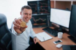 Businessman holding bitcoin in hand while sitting in modern office with many monitors with graphs photo