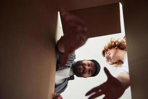 hombre barbudo tratando de alcanzar el artículo de una caja. pareja feliz juntos en su nueva casa. concepción de movimiento foto