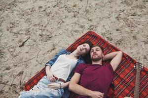 Looking up. Young couple have picnic on the beach. Lying on the red colored blanket photo