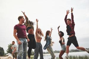 emocionados jóvenes amigos. grupo de personas hacen picnic en la playa. divirtiendose el fin de semana foto