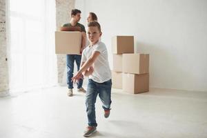 In front of parents. Playful mood from the kid. Family have removal into new house. Unpacking moving boxes photo