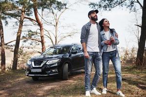 chico barbudo abrazando a su novia. abrazar y disfrutar de la naturaleza. una pareja ha llegado al bosque en su nuevo auto negro foto